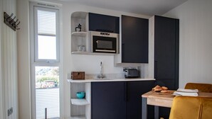 A compact kitchen with dark cabinetry, a microwave, and a window overlooking a street. - Rosthwaite  Woodland pod - a holiday Pod that sleeps 2 with an en-suite (Winster)