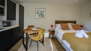 A compact hotel room with a bed, bedside table, and a small kitchenette. - Rosthwaite  Woodland pod - a holiday Pod that sleeps 2 with an en-suite (Winster)