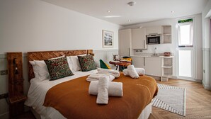 Hotelkamer met een groot bed, houten hoofdeinde, een kitchenette en een raam met zonwering.