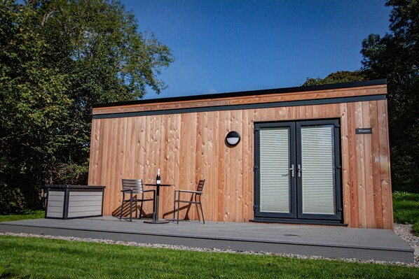 A modern wooden building with a sliding glass door, a small outdoor seating area with two chairs and a table, and a sign that reads "Winster".