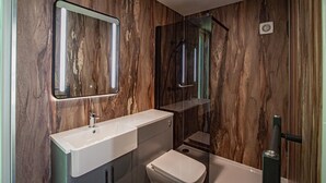 Een badkamer met een marmeren wand, een wit wastafel, toilet en een douche met glazen wanden.