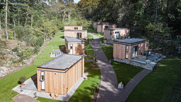 Een groep houten vakantiehuisjes met een pad in het midden, omringd door weelderige begroeiing en bomen.