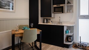Une cuisine moderne avec des meubles de couleur noire, une table à manger en bois et une fenêtre équipée de stores.