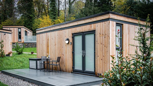 Une cabane moderne en bois, dotée d’une terrasse, d’une table et de chaises, ainsi que d’une porte coulissante.