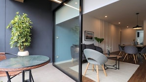 A modern living space with a glass partition, a round glass table, wicker chairs, a grey upholstered chair, and a potted plant. - w* | Fantastic 2BR with Balcony in Miraflores (Miraflores)