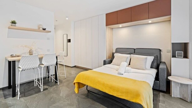 Un dormitorio moderno con cama, mesitas de noche, un escritorio con sillas y armarios empotrados.