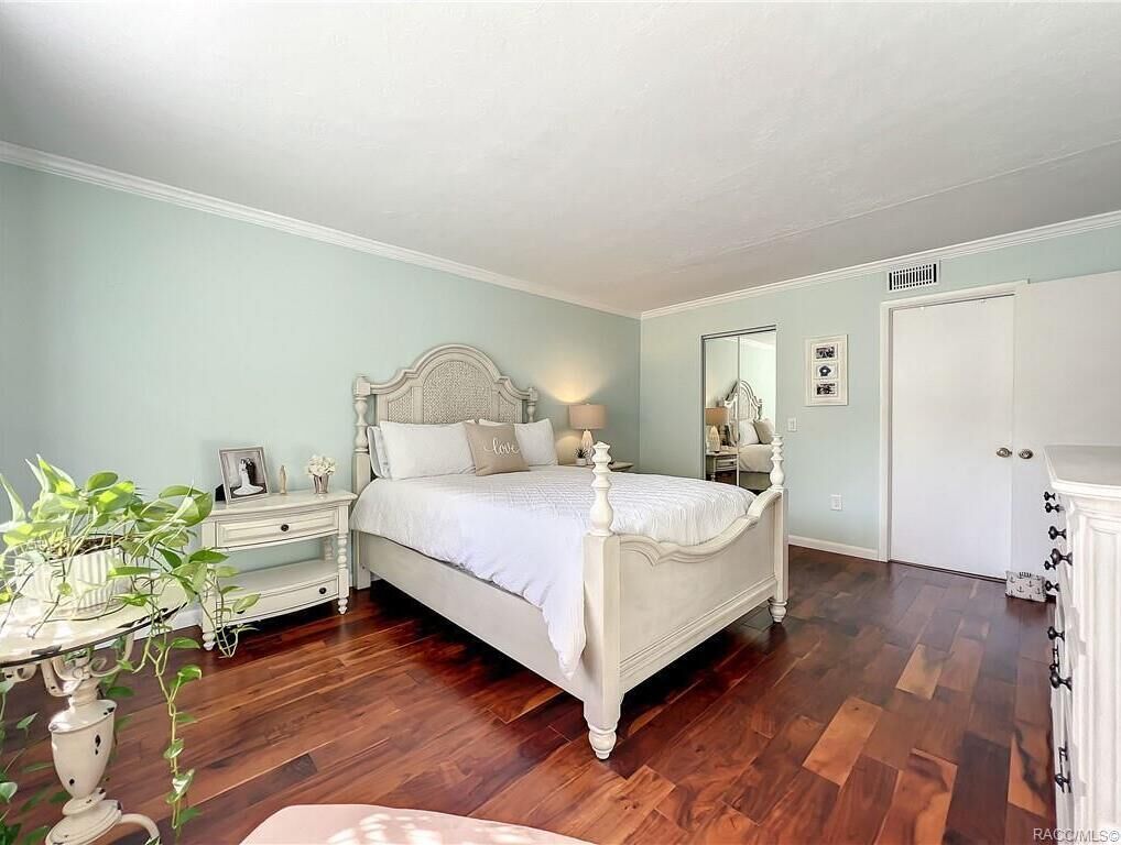 Un dormitorio con una cama con dosel blanco, una mesita de noche con lámpara, una mesita auxiliar y un aparador.