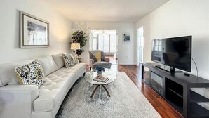 En moderne stue med sofa, sofabord, fjernsyn og udsigt til det fri.