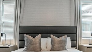 A neatly made bed with a headboard, two bedside tables, and a window with curtains.