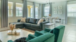A modern living room with a sectional sofa, a coffee table, and a dining area with a white table and chairs.