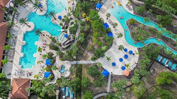 An aerial view of a resort with multiple swimming pools, palm trees, and lounge areas.