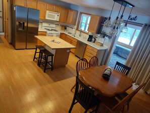 A kitchen with wooden cabinets, a stainless steel refrigerator, a microwave, a gas stove, and a dining area with a wooden table and chairs. - Be Blessed at Kinship Casa in Rome, WI (Nekoosa)
