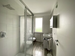 A modern bathroom with a glass shower enclosure, a toilet, a sink, and a window providing natural light. - Villa Gioia, with a pool in Monferrato (Piemonte)