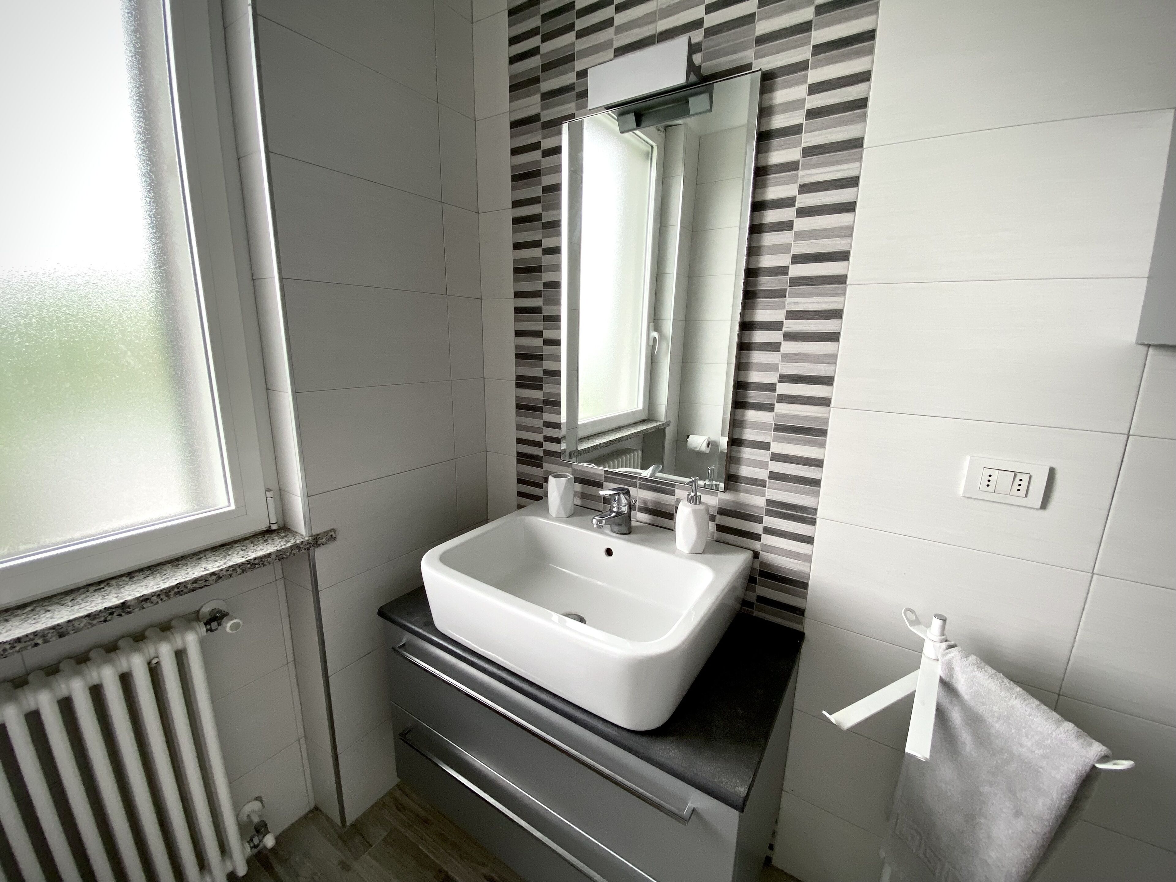 Een badkamer met een wit wastafelmeubel, een spiegel, een handdoekhouder en een raam.