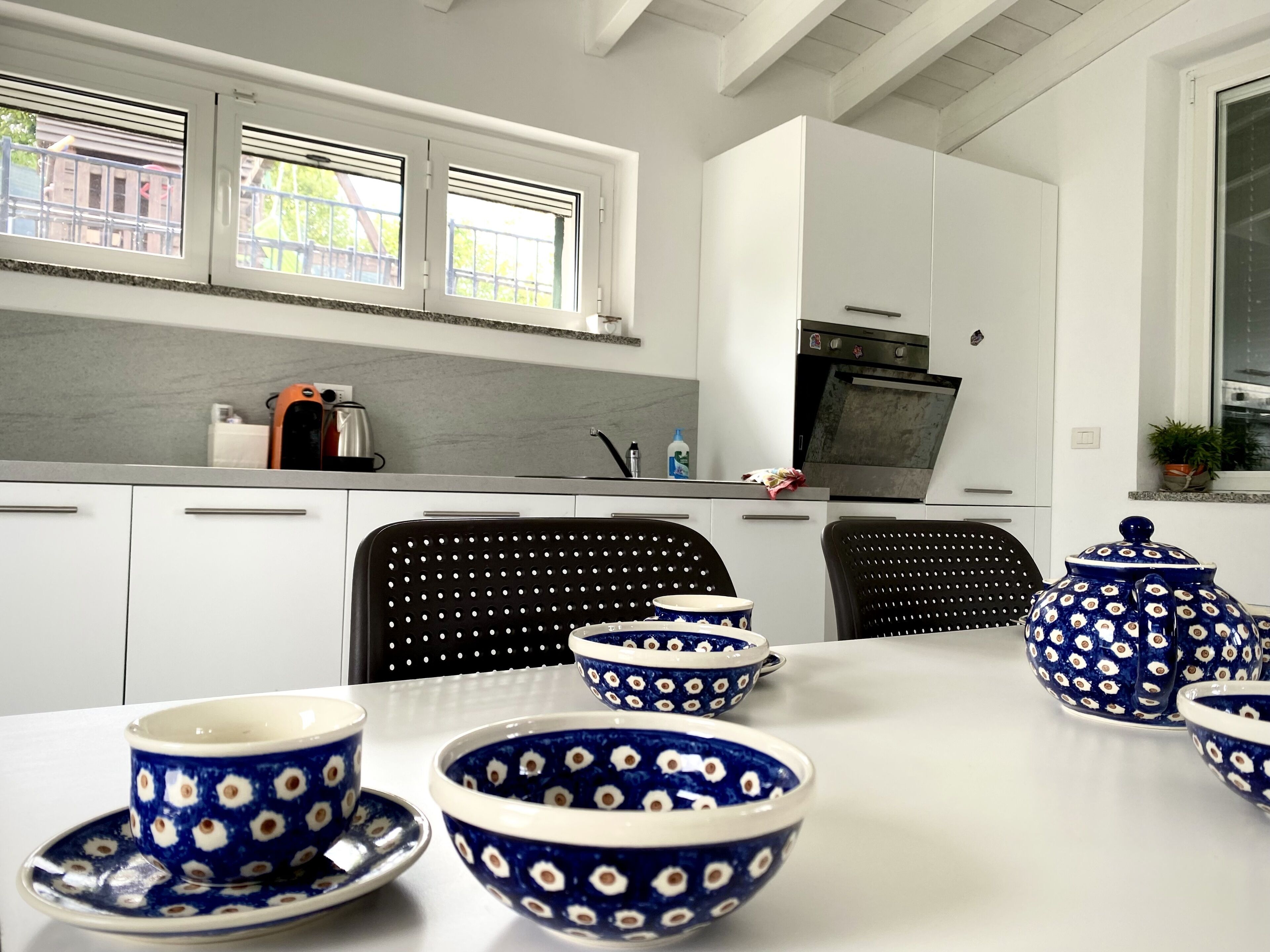 A modern kitchen with white cabinets, a black chair, and blue and white patterned bowls on the table.
