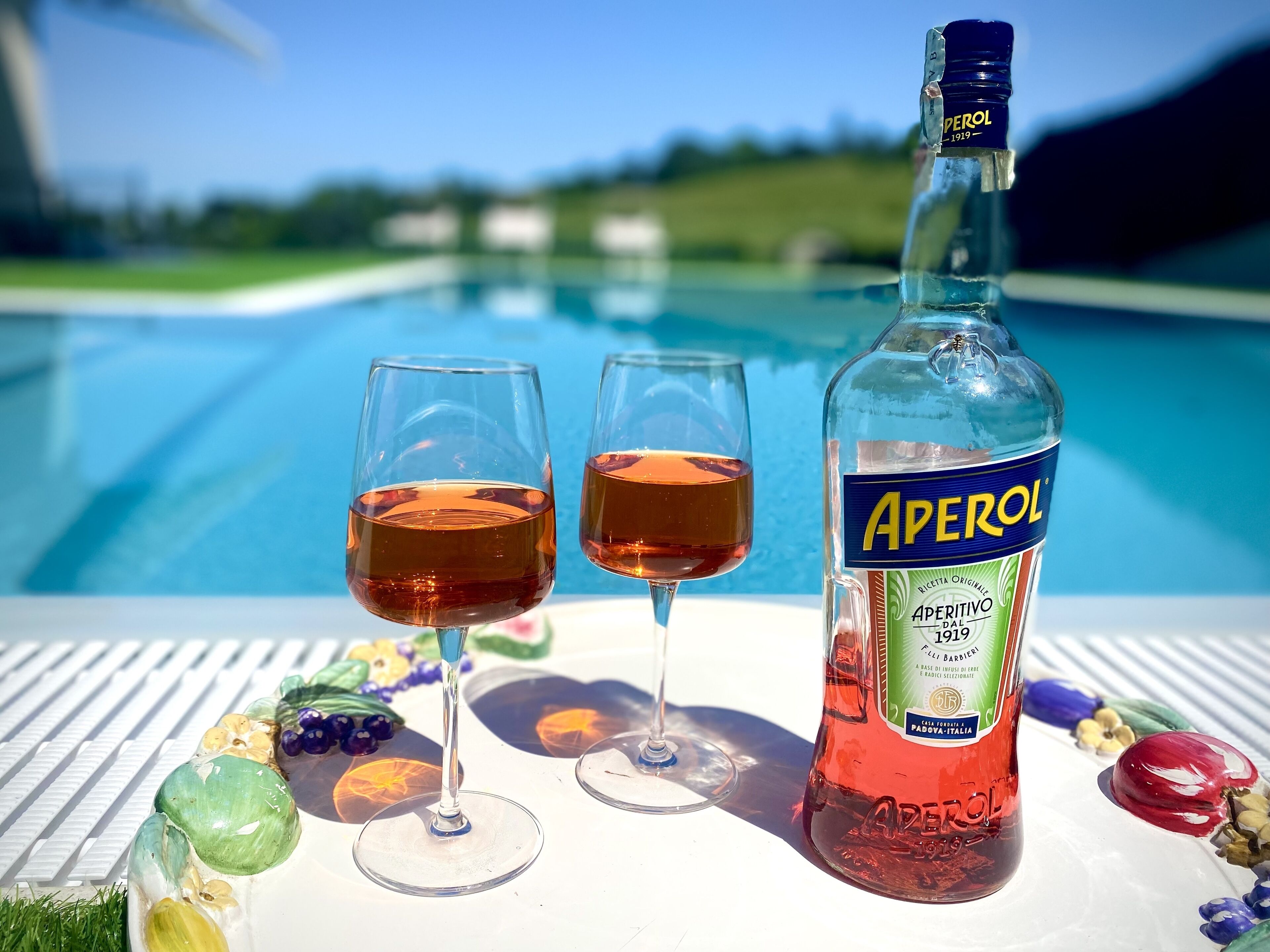 Eine Aperol-Flasche mit zwei Gläsern des Getränks auf einem Tisch am Pool.