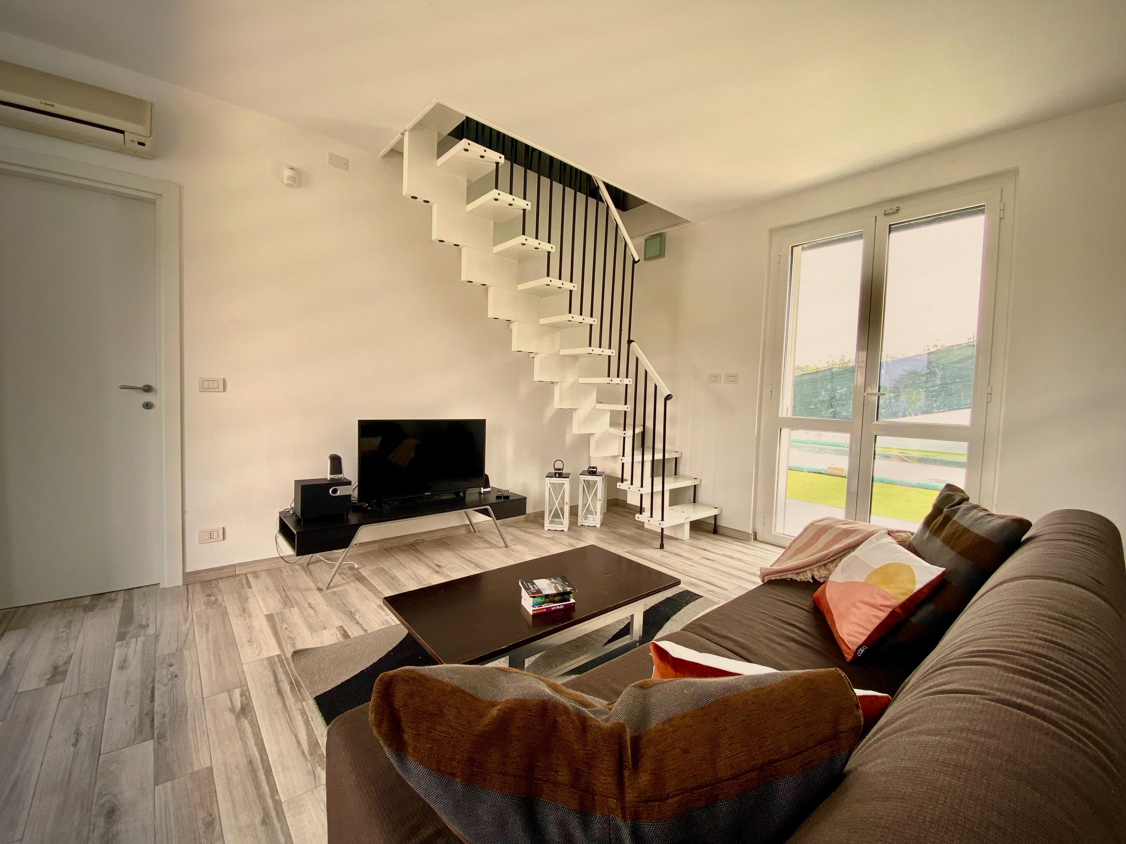 A modern living room with a staircase, a flat-screen TV, a coffee table, and a sofa.