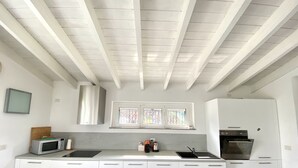 Una cucina moderna con mobili bianchi, una cappa in acciaio inossidabile, una finestra sopra il lavello e un forno a microonde sul piano di lavoro.