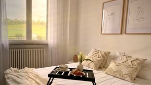 Una camera da letto con un letto, un comodino, una finestra con tende e due quadri appesi al muro.