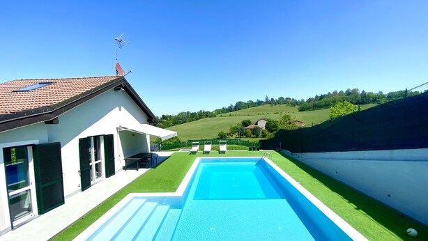 Una casa moderna con piscina, veranda coperta e vista su un paesaggio verde.