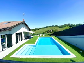 A modern house with a swimming pool, a covered patio, and a view of a green landscape.