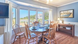 A dining area with a table set for four, surrounded by wooden chairs, a ceiling fan, and a view of the outdoors. - Dogs Ok, Large Deck, BBQ, Fire pit, Close to Beach (Brock) (Long Beach)