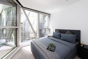 A modern bedroom with a large window, a bed with grey bedding, and a small plant on the bed. - A Cozy 2BR Apt for 6 Next to Southern Cross (Melbourne)