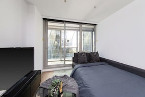 A modern bedroom with a large bed, a flat-screen TV, and a sliding glass door leading to a balcony. - A Cozy 2BR Apt for 6 Next to Southern Cross (Melbourne)