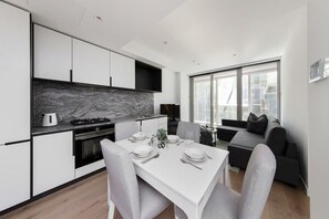 Een moderne keuken met witte kastjes, een marmeren achterwand en een eethoek met een witte tafel voor vier personen.