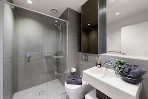 A modern bathroom with a glass-enclosed shower, a white toilet, and a sink with a mirror above it. - A Cozy 2BR Apt for 6 Next to Southern Cross (Melbourne)