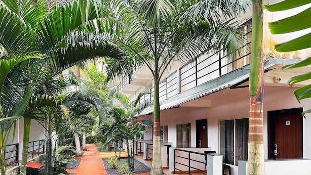 A corridor with a red pathway flanked by palm trees and small plants, leading to a building with a balcony and a door marked '401'. - Bay Breeze Hotels & Resorts (Morjim)