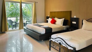 A hotel room with a large bed, a smaller bed, a balcony with a chair, and a view of greenery outside. - Bay Breeze Hotels & Resorts (Morjim)