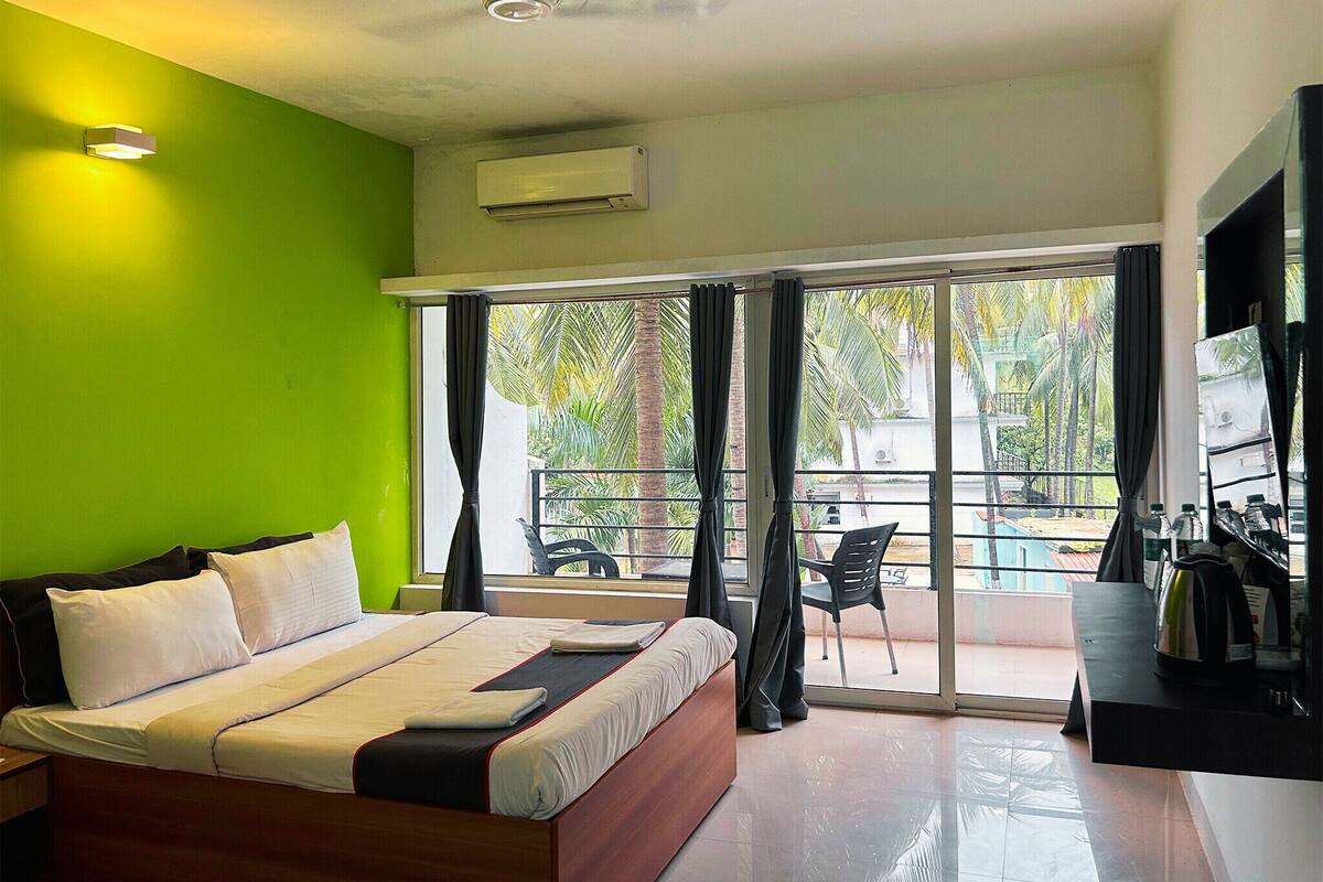 Habitación de hotel con cama, escritorio, silla, ventilador de techo y vistas a una piscina y palmeras.