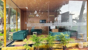 A modern interior with glass walls, a wooden ceiling, and a seating area with green sofas. - Bay Breeze Hotels & Resorts (Morjim)