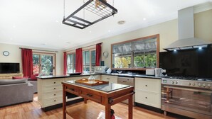A modern kitchen with wooden flooring, a central island, a built-in oven, and a dining area with a sofa.