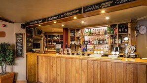 Zona de bar con paneles de madera, diversas botellas de licores y una pizarra que muestra el menú de café y comida.