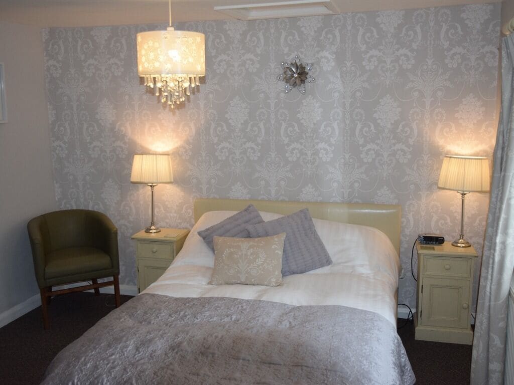 A neatly arranged bedroom with a bed, two bedside lamps, a chair, and a decorative wall piece.