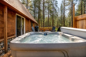 A hot tub in a forested area with a wooden cabin and outdoor seating.