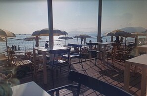 Un restaurant situé en bord de mer, avec une terrasse et des parasols, offrant une vue sur l’océan.