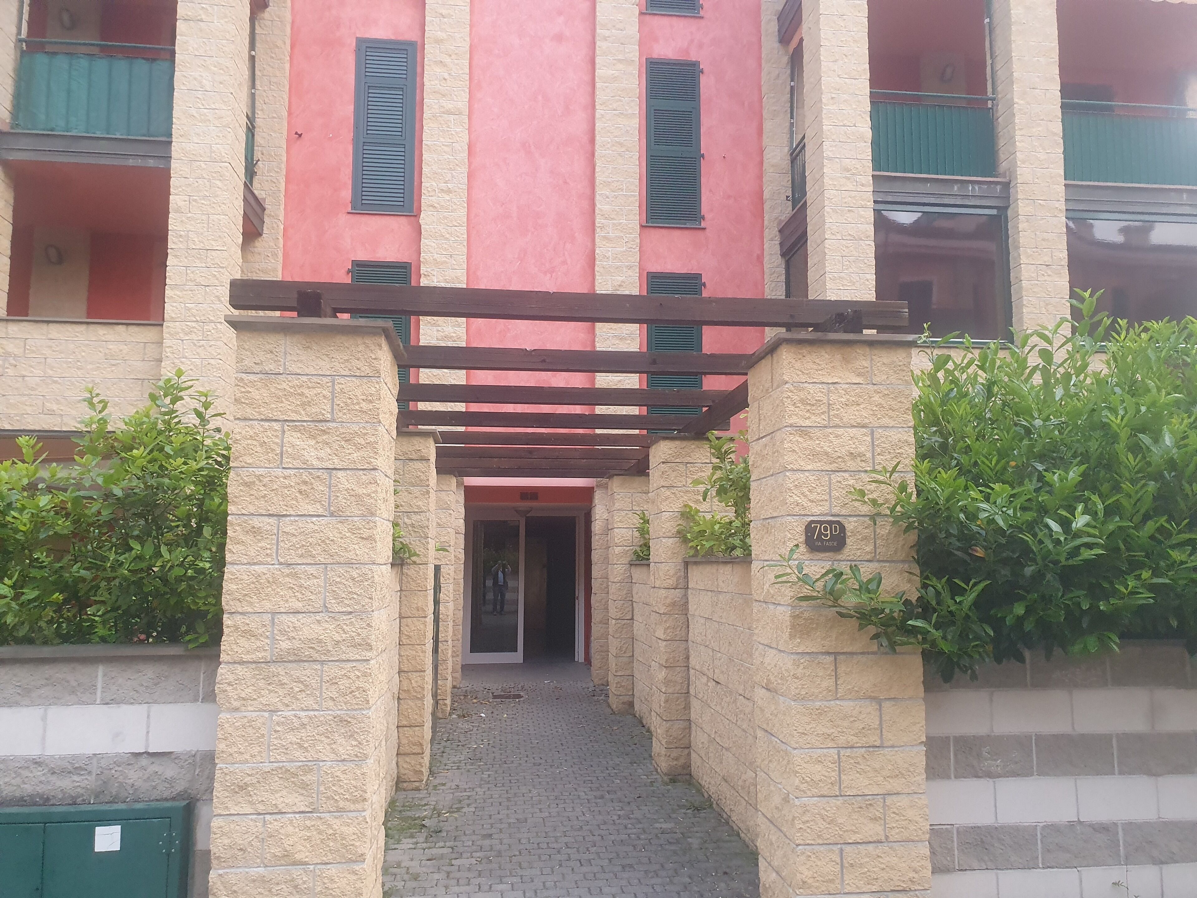 Un estrecho callejón que conduce a un edificio con fachada roja y contraventanas verdes.