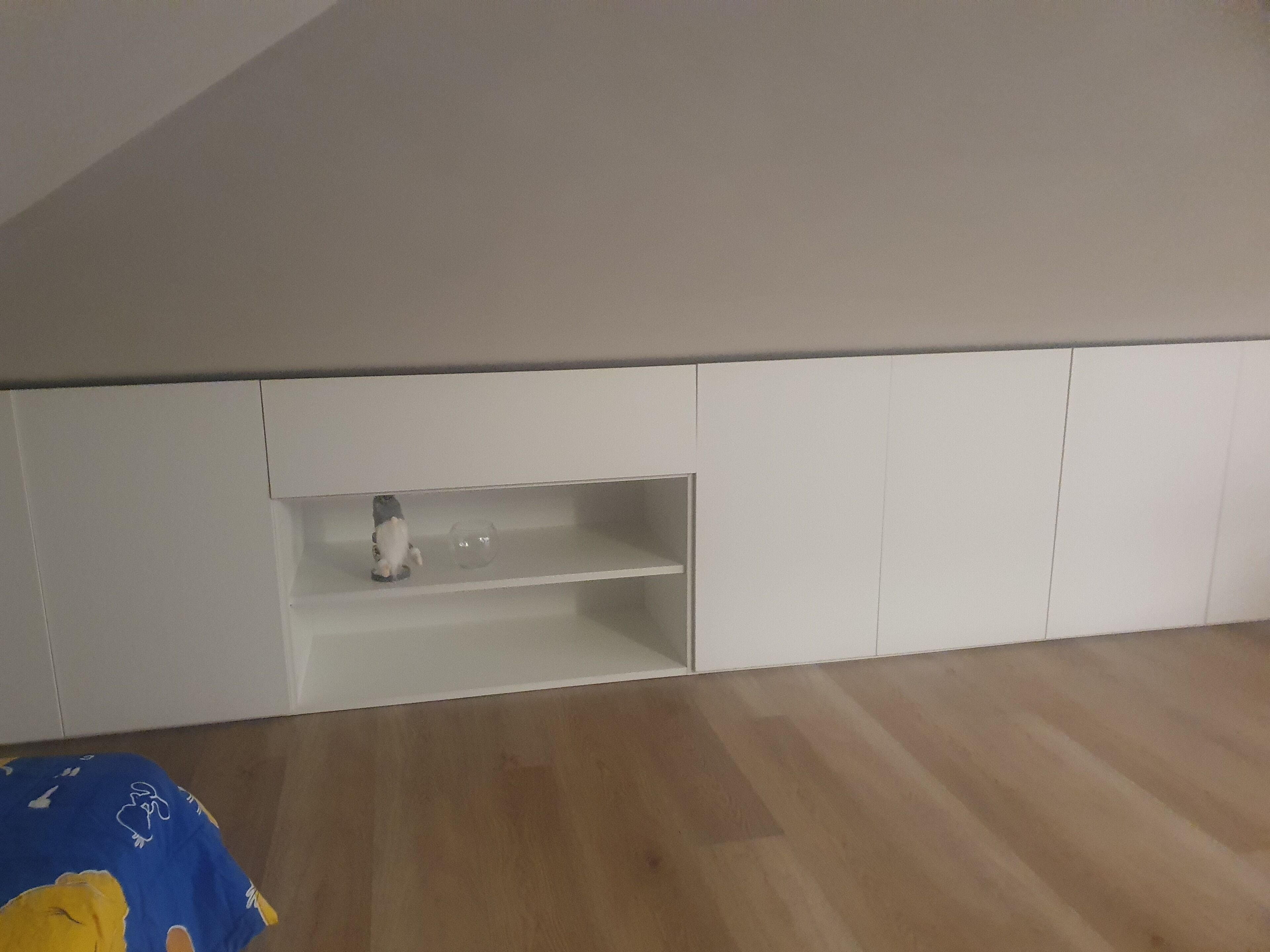 A room with a sloped ceiling, white built-in cabinets, and a wooden floor.