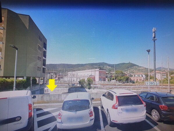 Un parking avec plusieurs voitures, un bâtiment avec une porte rouge et un paysage montagneux en arrière-plan.
