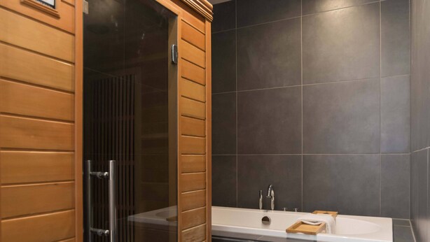 A modern bathroom with a glass-enclosed steam shower, a white sink, and dark tiled walls.