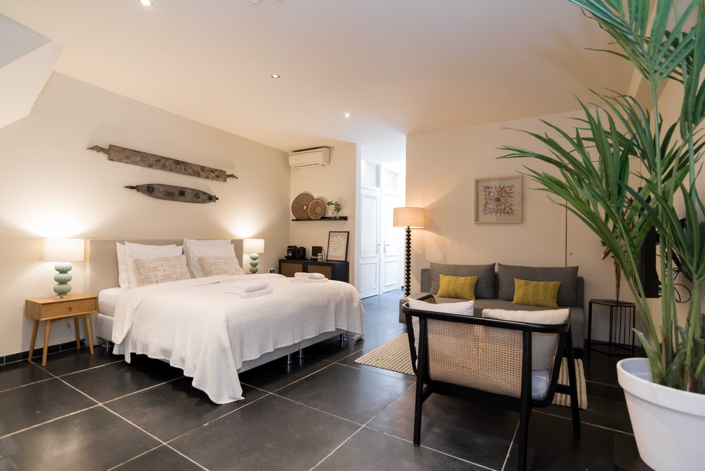 Une chambre moderne avec un grand lit, des tables de chevet, un coin salon avec un fauteuil et une plante en pot.