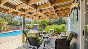 En overdækket udendørs terrasse med swimmingpool, fletmøbler og træloft.