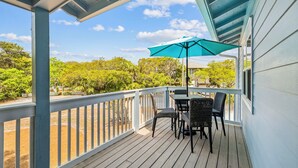 En overdækket terrasse med et bord og stole, en blå parasol og udsigt til grøn vegetation og et hus.