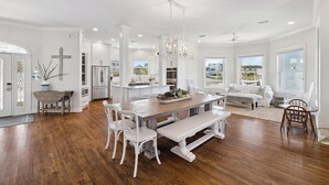 Una cocina amplia con armarios blancos, un comedor con una mesa de madera y sillas blancas, y un ventanal con vistas al exterior.