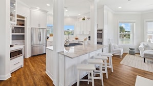 Una cocina moderna con muebles blancos, un refrigerador de acero inoxidable y una isla central con taburetes de bar.