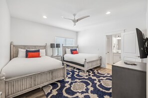 Une chambre d’hôtel avec deux lits, un ventilateur de plafond, un bureau avec un téléviseur à écran plat et un tapis à motifs.