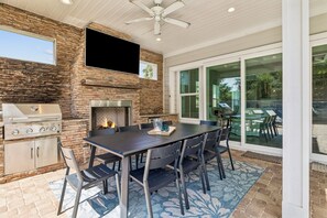 Un espace patio agrémenté d’un mur en pierre, d’un barbecue, d’une table avec des chaises et d’un ventilateur de plafond.